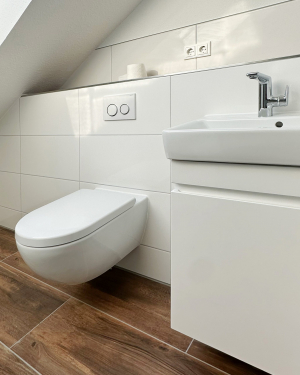 Kleines Badezimmer groß gedacht mit Holzfliesenboden, weißen Wandfliesen, Waschtisch mit Chrom-Armatur, weißem Waschtischunterschrank, Hänge-WC und Dampfdusche – funktionales und stilvolles Design. Petri Heizung &amp; Sanitär, Mühlheim am Main.