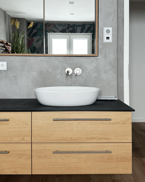 Badezimmer in Betonoptik mit Holzfliesenboden, barrierefreier Dusche mit Regenduschsystem, altersgerechten Sitzmöglichkeiten und Aufsatz-Waschbecken mit Holz-Waschtischunterschrank für stilvolles, funktionales Design. Petri Heizung &amp; Sanitär, Mühlheim am Main