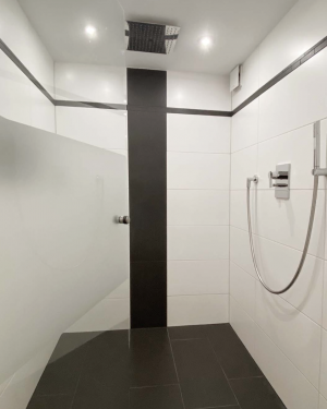 Zeitloses Badezimmer mit schwarzen Bodenfliesen, weißen Wandfliesen, Badewanne, barrierefreier Dusche mit Regenduschsystem, Toilette, Bidet und Wandheizkörper für elegantes und modernes Design. Petri Heizung &amp; Sanitär, Mühlheim am Main