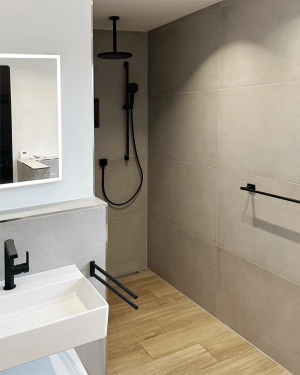 Badezimmer mit dunkelgrauen Wandfliesen, Holzfliesenboden, weißem Waschbecken mit Spiegel, barrierefreier Dusche mit Regenduschsystem, schwarzer Armatur, Handtuchhalter, WC-Drückerplatte und Wandheizkörper für stilvolles und funktionales Design. Petri Heizung &amp; Sanitär, Mühlheim am Main