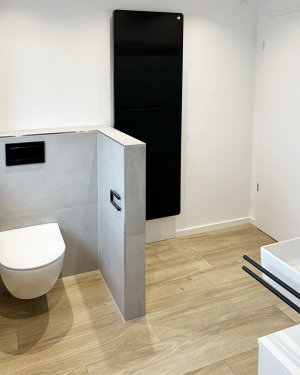 Badezimmer mit dunkelgrauen Wandfliesen, Holzfliesenboden, weißem Waschbecken mit Spiegel, barrierefreier Dusche mit Regenduschsystem, schwarzer Armatur, Handtuchhalter, WC-Drückerplatte und Wandheizkörper für stilvolles und funktionales Design. Petri Heizung &amp; Sanitär, Mühlheim am Main