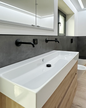 Modernes Badezimmer mit anthrazitfarbenen Wandfliesen, Holzfliesenboden, Waschtischunterschrank aus Holz, großem Doppelwaschtisch, schwarz-matte Armaturen, Toilette, Bidet, Badewanne und barrierefreier Dusche mit Regenduschsystem für stilvolles und funktionales Design.