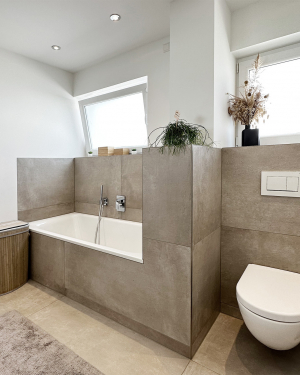 Badezimmer mit betonfarbenen Fliesen, Badewanne, WC, bodentiefer Dusche mit Regenduschsystem, Waschbecken mit weißem Waschtischunterschrank, Chrom-Armaturen und einem eleganten Wandheizkörper für zeitloses, funktionales Design und stilvolles Wohlfühlbad. Petri Heizung &amp; Sanitär, Mühlheim am Main