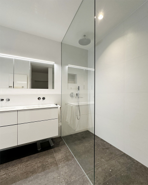 Helles Badezimmer mit anthrazitfarbenen Bodenfliesen, weißen Wandfliesen, barrierefreier Dusche mit Regenduschsystem, Badewanne, Doppelwaschtisch mit Chrom-Armatur, Spiegel, Toilette und modernen Sanitärinstallationen, elegantes und funktionales Design. Petri Heizung &amp; Sanitär, Mühlheim am Main.