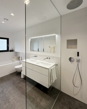 Helles Badezimmer mit anthrazitfarbenen Bodenfliesen, weißen Wandfliesen, barrierefreier Dusche mit Regenduschsystem, Badewanne, Doppelwaschtisch mit Chrom-Armatur, Spiegel, Toilette und modernen Sanitärinstallationen, elegantes und funktionales Design. Petri Heizung &amp; Sanitär, Mühlheim am Main.