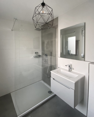 Helles Badezimmer mit Wandheizung, nahezu bodenebener Dusche mit Regenduschsystem, Waschtisch mit Chrom-Armatur, Spiegel und modernen Sanitärinstallationen, elegantes und funktionales Design. Petri Heizung &amp; Sanitär, Mühlheim am Main.