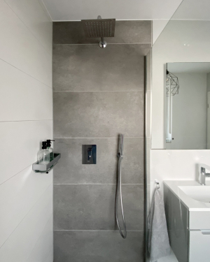 Helles Badezimmer mit Wandheizung, nahezu bodenebener Dusche mit Regenduschsystem, Waschtisch mit Chrom-Armatur, Spiegel und modernen Sanitärinstallationen, elegantes und funktionales Design. Petri Heizung &amp; Sanitär, Mühlheim am Main.
